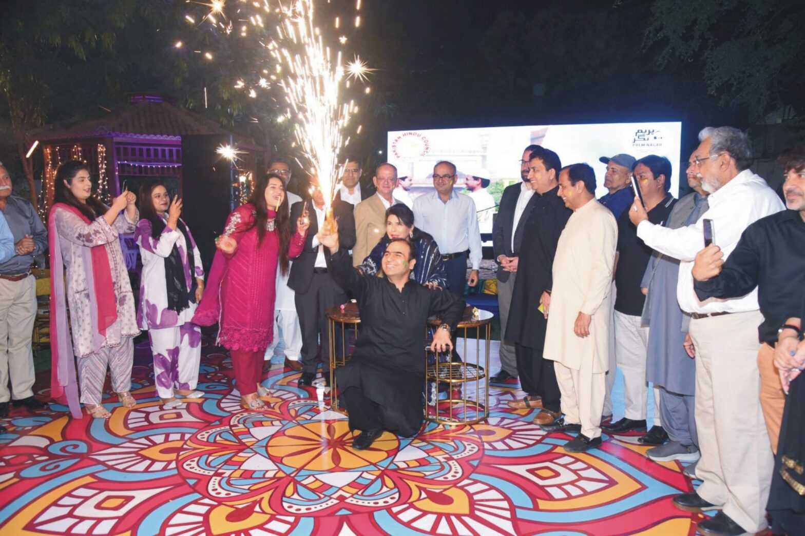 Dr. Ramesh Kumar Vankwani standing among guests during a festive celebration of Holi and Eid with fireworks, cultural performances, and traditional cuisine.